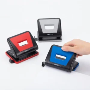 Perforateur 2 trous Deli en trois coloris rouge, gris et bleu à bases noires, posés sur fond blanc, une main en action